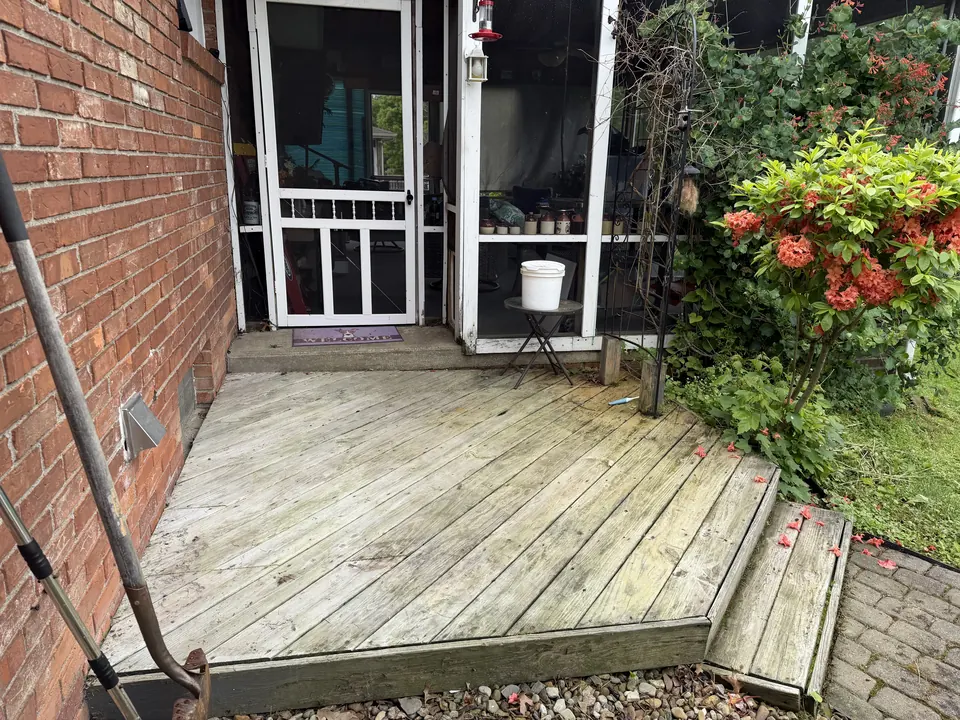 Weathered, splintering wood stoop outside a brick home's screen porch before replacement